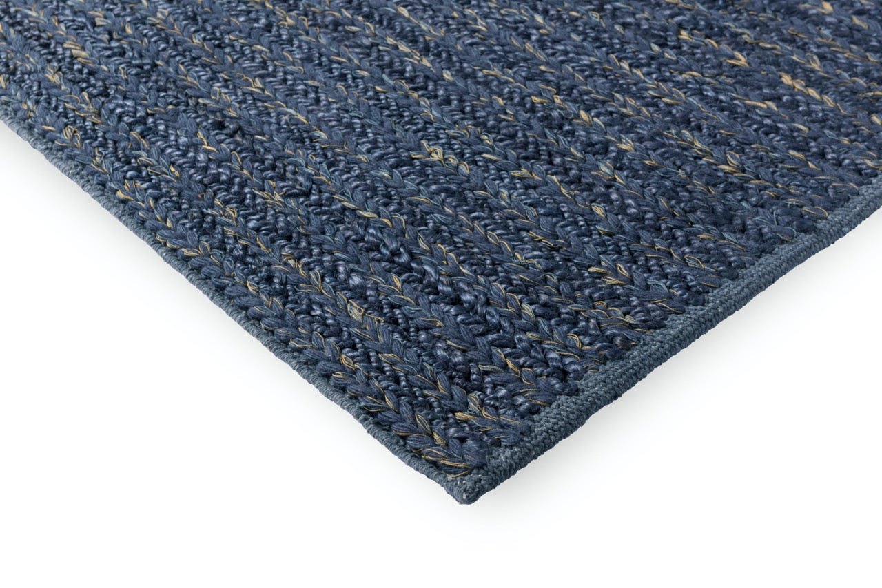 Corner view of blue braided wool rug on pale wood floor showing weave height