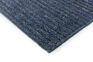 Corner view of blue braided wool rug on pale wood floor showing weave height