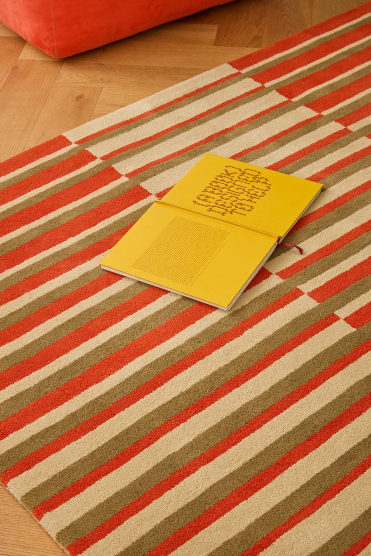 Brink & Campman Decor Pilar Coral rug in coral red with olive green and cream stripes, shown in an interior, second view