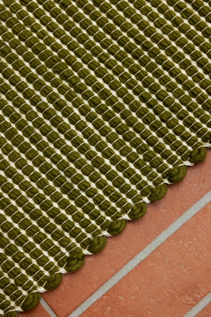 Close-up of green wool and jute weave with ivory edge stitch and soft texture