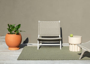 Brink & Campman Lace Thyme Pine rug placed under outdoor seating on a tiled terrace with wood and linen accents